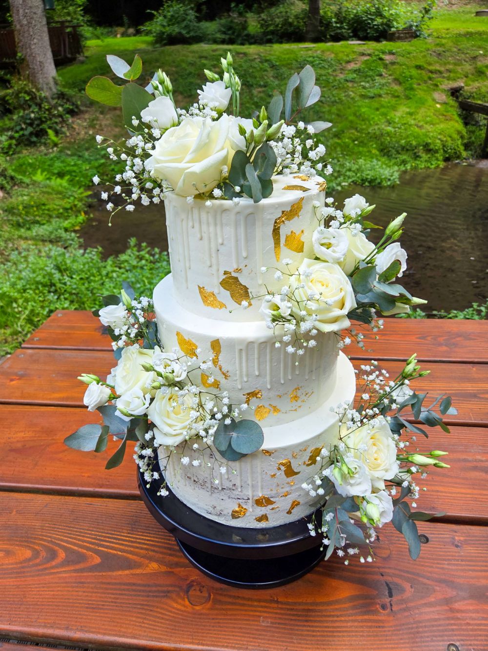 Dreitstöckige Hochzeitstorte mit Rosen und Eukalyptusblättern verziert mit Gold